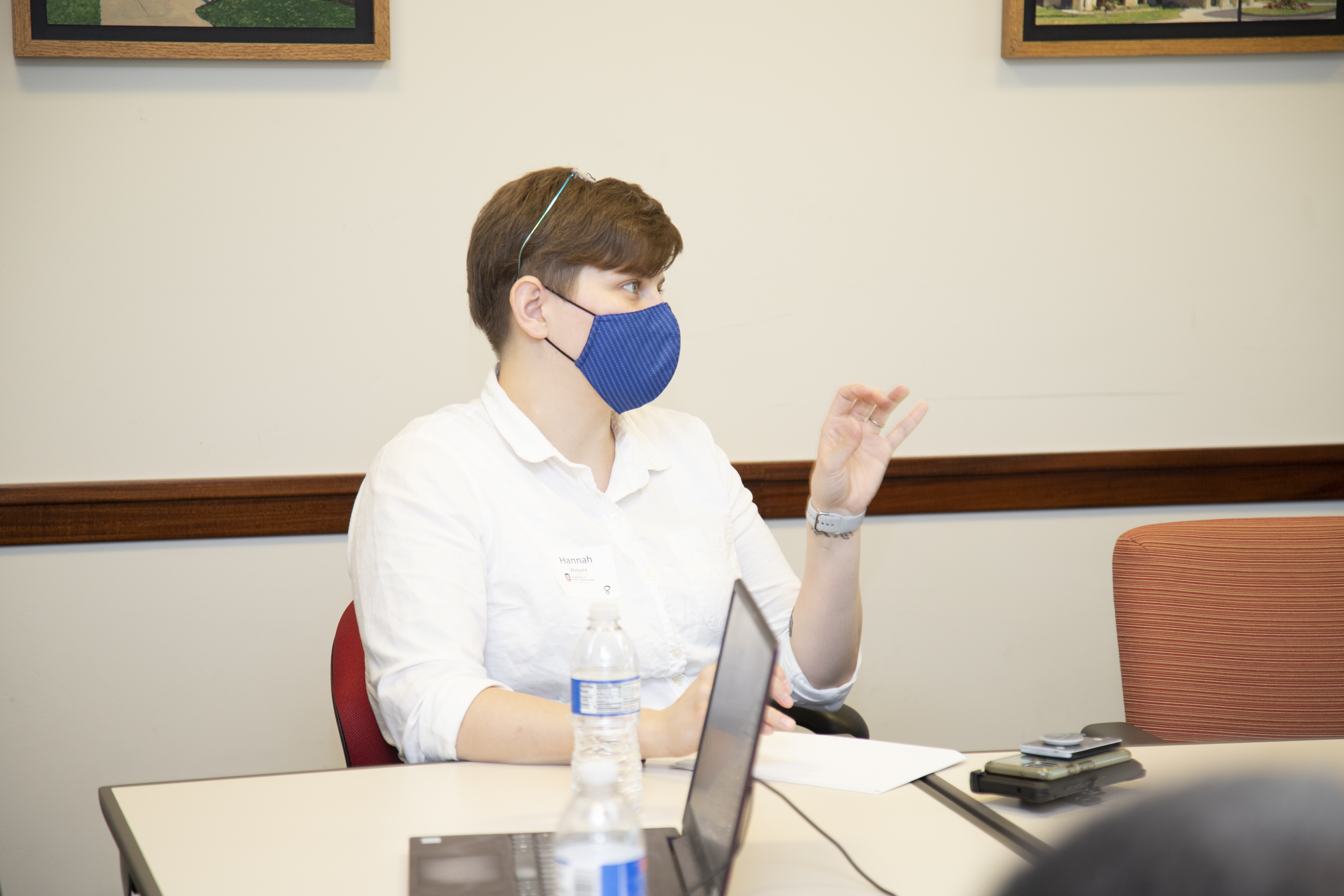 A female presenting person wearing a face mask appears to be in a meeting and is gesturing while speaking.